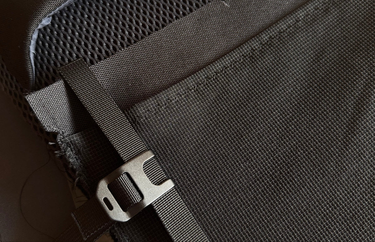 Close-up of a black backpack showing the interior mesh lining, a black webbing strap, and a silver metal buckle.